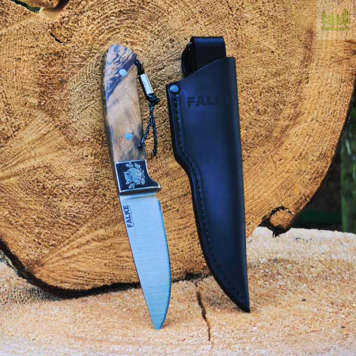 Nóż myśliwski Falke JF30-2 na pieńku z czarną skórzaną pochwą Ręcznie robiony nóż myśliwski Falke JF30-2 ze stali N690, zaprezentowany na pieńku w naturalnym otoczeniu. Widoczna skórzana pochwa w kolorze czarnym